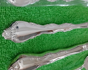 May include: Two silver-plated spoons with ornate designs on a green background.