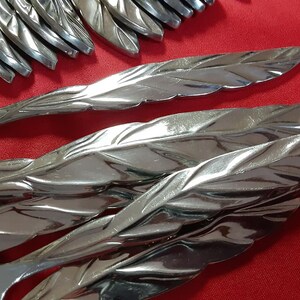 May include: A set of silver flatware with a leaf design. The flatware is arranged in a pile, with the handles facing up. The flatware is shiny and reflects the light.
