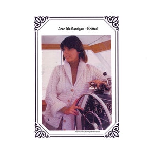 May include: A vintage image of a white Aran Isle cardigan, knitted. The cardigan has a textured cable knit design, a shawl collar, and button closures. The image is framed with a decorative border and includes the text "Aran Isle Cardigan - Knitted".