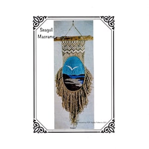 May include: A macrame wall hanging featuring a seagull design. The artwork includes a central oval with a blue sky and a flying seagull, with a landscape below. The piece is framed with a decorative border and the text "Seagull Macrame".