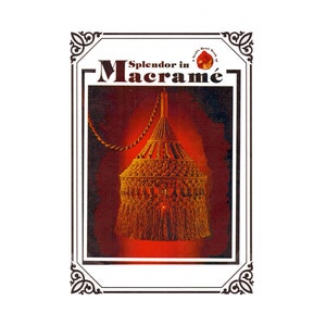 May include: A framed image featuring a macramé lampshade. The lampshade is a warm, golden color, with a fringed bottom. The text "Splendor in Macramé" is displayed above the lampshade, within a decorative frame.