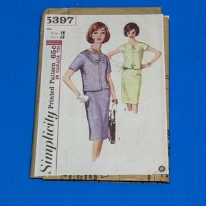 May include: A vintage Simplicity sewing pattern envelope, number 5397, size 18, bust 38. The front features an illustration of a two-piece outfit with a short-sleeved top and a skirt in two color variations, purple and light green, with a small bow detail.