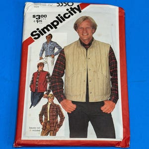 May include: A vintage Simplicity sewing pattern packet featuring a man wearing a quilted vest over a plaid shirt. The packet has a red border and the word "Simplicity" in a bold, angled font.