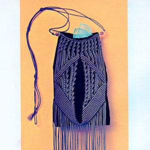 Peut inclure: Un sac noir en macramé avec un long fond à franges. Le sac présente un motif tissé dans des tons de bleu et un long cordon pour le porter à l'épaule. La frange se termine par de petits pompons et des perles.