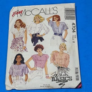 May include: A white McCall's sewing pattern envelope for size 8 blouses, labeled 4704 Fashion Basics. The front features illustrations of six different blouse styles, including solid, striped, and polka-dot designs, with various sleeve lengths and necklines.