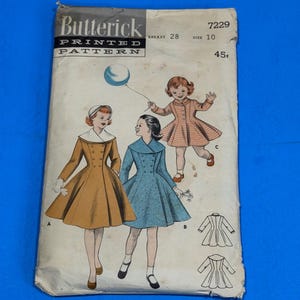 May include: Vintage Butterick printed sewing pattern. The pattern features illustrations of dresses in mustard yellow and blue, with a child's dress in a pink and white check. The pattern number is 7229, with a breast size of 28 and size 10.