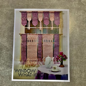 May include: A vintage image showing macrame window hangings in purple and beige. The image includes a window with the macrame curtains, a small table with a teapot, teacup, and a candle. The text "WINDOW WHAT-KNOT" is at the bottom.