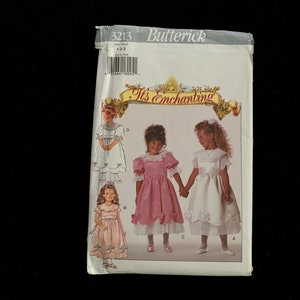 May include: A Butterick sewing pattern packet, featuring illustrations of little girls in dresses. The packet is white with the text "It's Enchanting" and the number 3213. The dresses are pink and white.