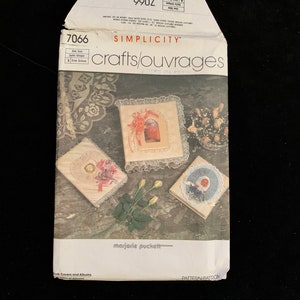 May include: Simplicity crafts pattern 7066 for book covers and albums. The package features images of decorated book covers with lace, ribbons, and floral accents. The package is white with red text and the words "crafts/ouvrages".