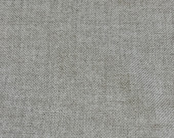 Può includere: Primo piano di un tessuto strutturato grigio chiaro. La trama del materiale è visibile, creando un motivo sottile. Il tessuto sembra essere una fibra naturale, forse lino o un materiale simile, con una consistenza leggermente ruvida.