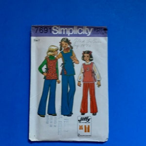 May include: Vintage Simplicity sewing pattern featuring three girls in 1970s-style outfits. The pattern includes designs for flared pants, vests, and tops. The pattern cover is white with the text "7691 Simplicity" and "Jiffy".