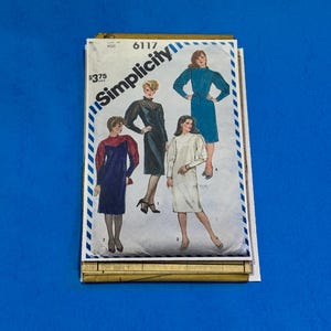 May include: A vintage Simplicity sewing pattern featuring illustrations of four different dress designs. The pattern packet is white with blue accents and the text "Simplicity" in a stylized font. The price is listed as $3.75.