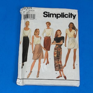 Può includere: Una busta per cartamodello Simplicity bianca, numero 9304, per le taglie 12, 14 e 16. Il fronte mostra illustrazioni di cinque diversi stili di gonna etichettati A, B, C, D ed E, abbinati a vari top, tra cui una gonna lunga nera e una gonna a fantasia.