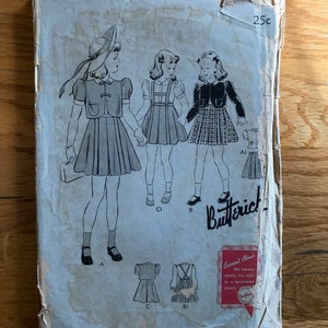 May include: Vintage Butterick sewing pattern envelope featuring illustrations of girls in dresses and jackets. The envelope is aged with visible wear and tear, and includes the price of 25c.