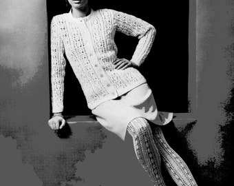 May include: A black and white image of a woman wearing a white, open-weave cardigan and skirt. She is also wearing patterned stockings. The cardigan has button closures. The woman is leaning against a dark background.