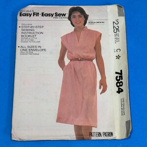May include: A McCall's Easy Fit Easy Sew pattern envelope for a dress, number 7584. The front features a photograph of a person wearing a pink, sleeveless, knee-length dress with a V-neckline and a brown belt. Text includes sewing instructions.