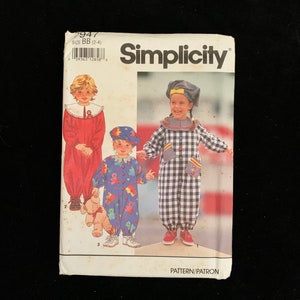 Puede incluir: Patrón de costura Simplicity para ropa de niños. El patrón presenta ilustraciones de tres conjuntos diferentes: un mono rojo, un mono azul con gráficos de osos y un mono a cuadros blanco y negro. La talla del patrón es BB (2-4).