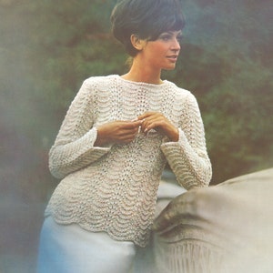 May include: A cream-colored, long-sleeved sweater with a scalloped design. The sweater has a crew neck and is worn with a light blue skirt. The image has a vintage aesthetic.