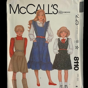 May include: McCall's sewing pattern envelope for a girl's jumper dress, size 8. The illustration shows three girls wearing different jumper dresses. The envelope is white with the McCall's logo and pattern number 8110.