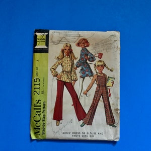 May include: Vintage McCall's 2115 sewing pattern for girls' dresses, blouses, and pants with bibs. The pattern cover features illustrations of girls in various outfits. The pattern is marked "Step-by-Step" and includes the size "7".