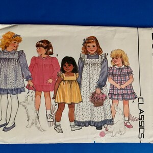 May include: A vintage Butterick Classics sewing pattern for girls' dresses, sizes 4-5-6. The pattern envelope features illustrations of girls in various dress styles, including floral, striped, and plaid designs. The envelope is white with a blue background.