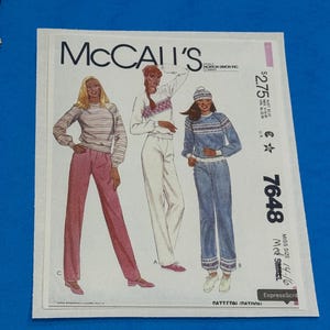 May include: A McCall's sewing pattern featuring illustrations of three different outfits: a striped top with pink pants, a white top with white pants, and a blue sweater with blue jeans. The pattern number is 7648, and the size is 14-16.
