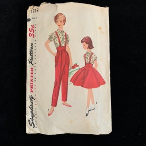 Könnte beinhalten: Vintage Simplicity Schnittmuster 1743 mit einer Frau und einem Mädchen in passenden Outfits. Die Outfits umfassen rote Hosen und einen Rock mit Hosenträgern, kombiniert mit einer Bluse mit Blumenmuster. Das Muster ist auf Papier gedruckt.