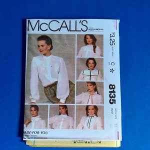 Puede incluir: Un patrón de costura vintage de McCall's con una mujer con una blusa blanca. El patrón incluye varios diseños de blusas con diferentes cuellos y adornos. El número de patrón es 8135, y el contorno de busto es de 91 cm.