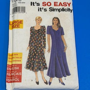 May include: A Simplicity sewing pattern envelope 7828 for large size dresses. The front shows two dress styles: one with a black background and colorful square patterns, and one solid purple dress. Text includes It's SO EASY it's Simplicity.