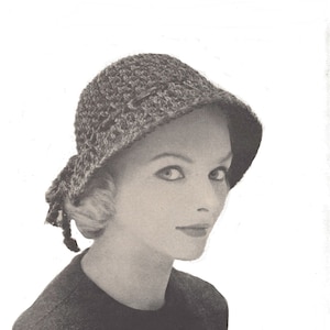 May include: A vintage black and white photograph of a woman wearing a crocheted cloche hat. The hat has a rounded crown and a small brim, with a decorative tie on the side. The woman is looking at the camera.