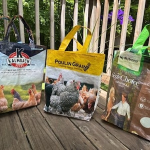 May include: Three reusable tote bags crafted from repurposed animal feed sacks. The left bag is blue and white with Kalmbach Feeds branding and chicken imagery. The center bag is yellow with Poulin Grain branding and chickens. The right bag is brown and green with Nutrena SafeChoice branding.