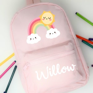 Może przedstawiać: Różowy plecak z płótna z motywem tęczy, słońca i chmur. Plecak ma kieszeń zapinaną na zamek błyskawiczny, a na przodzie nadrukowane jest imię "Willow".