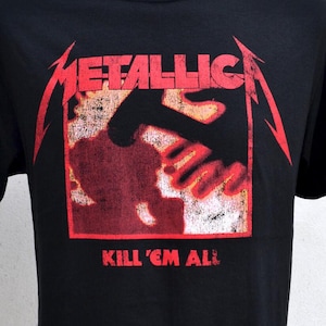May include: Black t-shirt with the red band name "METALLICA" and a red and orange hand graphic. The text "KILL 'EM ALL" is printed below. The t-shirt is displayed on a mannequin.
