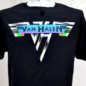 May include: Black t-shirt featuring the band name "Van Halen" in a colorful, retro design. The logo includes a triangle with a metallic finish. The shirt is displayed on a mannequin.
