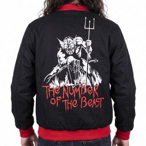 Può includere: Giacca bomber nera con colletto e polsini rossi. La schiena presenta una grafica bianca di un diavolo con un tridente, con il testo "THE NUMBER OF THE BEAST" in rosso.