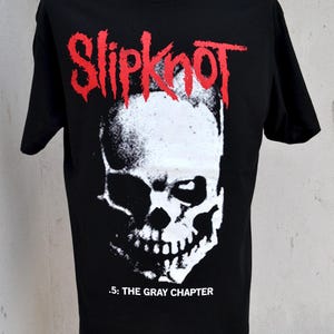 May include: Black t-shirt featuring a white skull graphic and the red band name "Slipknot" above it. Below the skull is the text ".5: THE GRAY CHAPTER". The shirt is displayed on a mannequin.