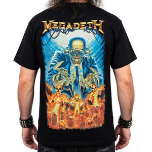 Può includere: Una t-shirt nera a maniche corte con una stampa grafica della band Megadeth. Il design mostra una figura scheletrica in abito blu con occhiali protettivi, posizionata sopra diverse figure arancioni luminose con simboli di radiazioni sulle teste.