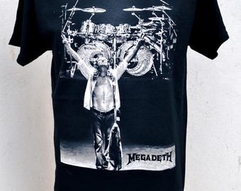 May include: Black t-shirt featuring a black and white image of a drummer with arms raised in front of a drum set. The band name "MEGADETH" is printed in white at the bottom of the image.
