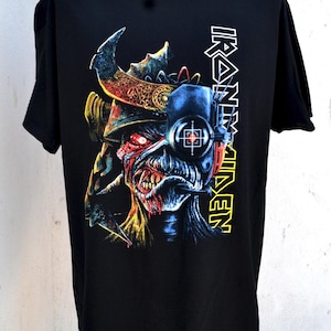 Op de afbeelding: Zwart t-shirt met een kleurrijke afbeelding van een monster met een helm en een vizier. Het woord "IRON MAIDEN" staat verticaal aan de rechterkant in wit en geel.