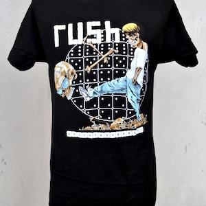May include: Black t-shirt featuring the band name "RUSH" in white block letters above a graphic of a skeleton figure kicking a domino. The phrase "ROLL THE BONES" is printed in white at the bottom of the design.