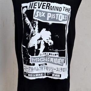 May include: Black sleeveless t-shirt with a Sex Pistols graphic and Japanese text. The design includes the words "NEVERMIND THE Sex Pistols" in white and grey. Japanese text reads "Rock history's worst event" and other Japanese text.
