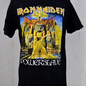 May include: Black t-shirt featuring the band name "Iron Maiden" in yellow lettering above a colorful graphic. The graphic depicts an Egyptian-themed scene with the word "Powerslave" in white below.