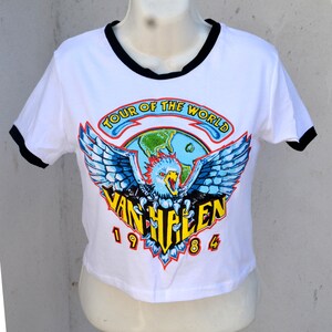 May include: White crop top with black trim featuring a colorful graphic. The graphic includes a blue eagle with outstretched wings, a globe, and the text "TOUR OF THE WORLD" and "VAN HALEN 1984".