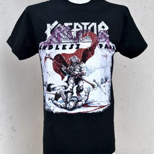 以下が含まれることがあります： 黒いTシャツ。バンド名「KREATOR」が白と紫の文字で、赤いマントと武器を持った戦士のグラフィックの上に書かれています。「ENDLESS PAIN」の文字がバンド名の下にあります。