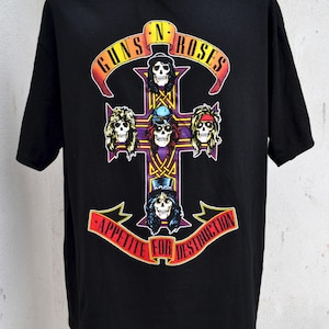Peut inclure: T-shirt noir avec le logo Guns N' Roses, représentant une croix de têtes de mort. Le nom du groupe est inscrit en arc de cercle en haut en jaune et rouge, avec "Appetite for Destruction" en bas.