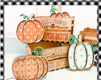 May include: Four wooden pumpkin cutouts with different patterns. The pumpkins are arranged in front of two wooden crates with the text "Farm Fresh Pumpkin Patch" on them.