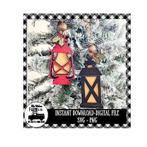 Könnte beinhalten: Zwei Holzlaternen-Anhänger, einer rot und einer schwarz, mit einem Stechpalmenzweig und einer Holzperle, die an jedem hängen. Die Anhänger hängen an einem schneebedeckten Weihnachtsbaumzweig. Der Text "INSTANT DOWNLOAD - DIGITAL FILE SVG - PNG" befindet sich am unteren Rand des Bildes.