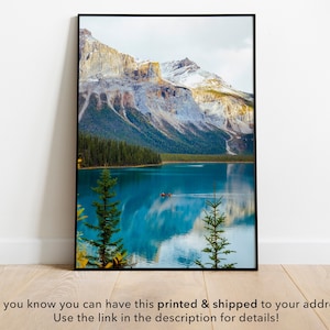 May include: A framed photograph of a mountain lake with snow-capped peaks and a reflection of the mountains in the water. The lake is a vibrant blue and the mountains are a light gray with snow on the peaks. There are trees on the shore of the lake.