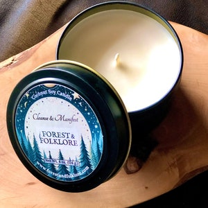 May include: A black candle tin with a white label that reads "Coconut Soy Candle Cleanse & Manifest FOREST & FOLKLORE Net Wt. 4 oz. (114 g.) www.forestandfolklore.com". The label has a forest scene with trees and a moon.