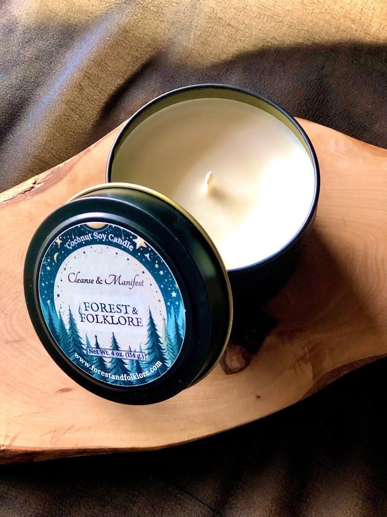 May include: A black candle tin with a white label that reads "Coconut Soy Candle Cleanse & Manifest FOREST & FOLKLORE Net Wt. 4 oz. (114 g.) www.forestandfolklore.com". The label has a forest scene with trees and a moon.